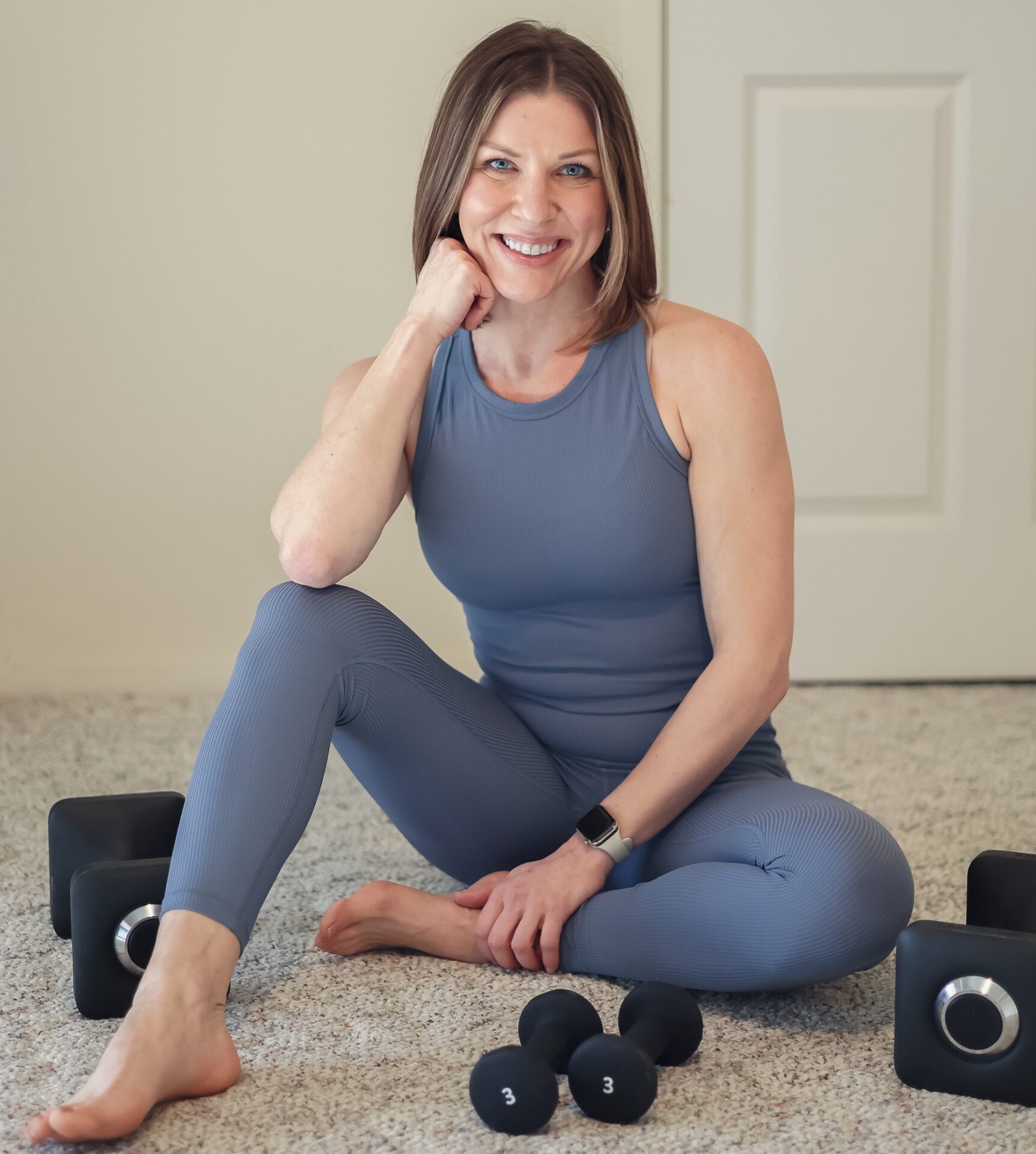 Jen sitting on the floor surrounded by small dumbbells