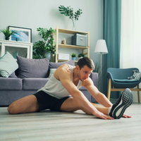 A man in his living room stretching his left hamstring on the floor