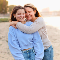a mom hugging her daughter on a beach and both are smiling